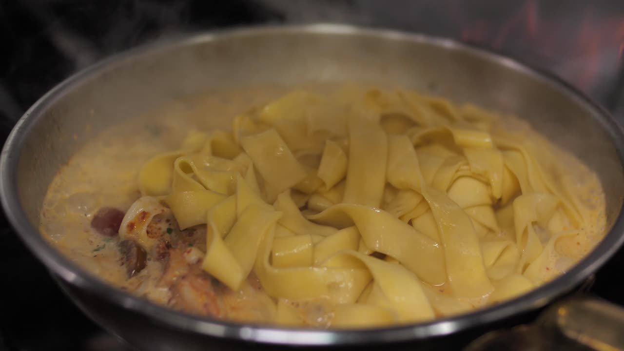 Fresh boiled pasta added to frying ragout on pan, close up