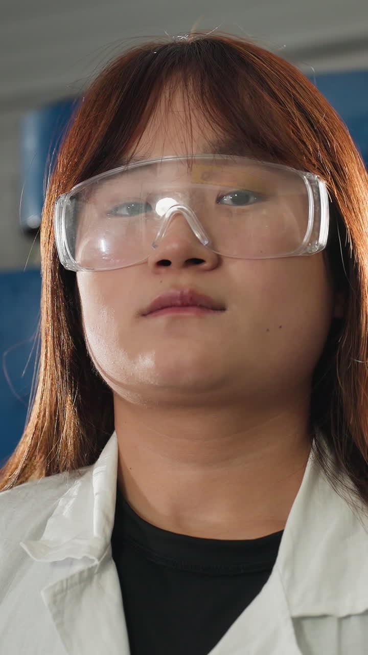 inventor en bata de laboratorio ajusta gafas de protección mientras inclina la cabeza hacia atrás en el taller de automóviles, coche negro y maquinaria visible en el fondo