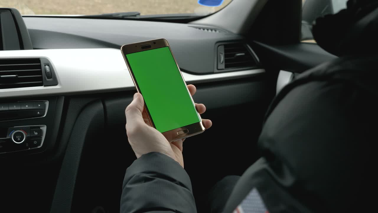 hombre de pantalla verde sosteniendo su teléfono inteligente en un coche
