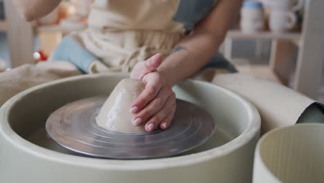 female potter shapes piece of clay on the pottery wheel.