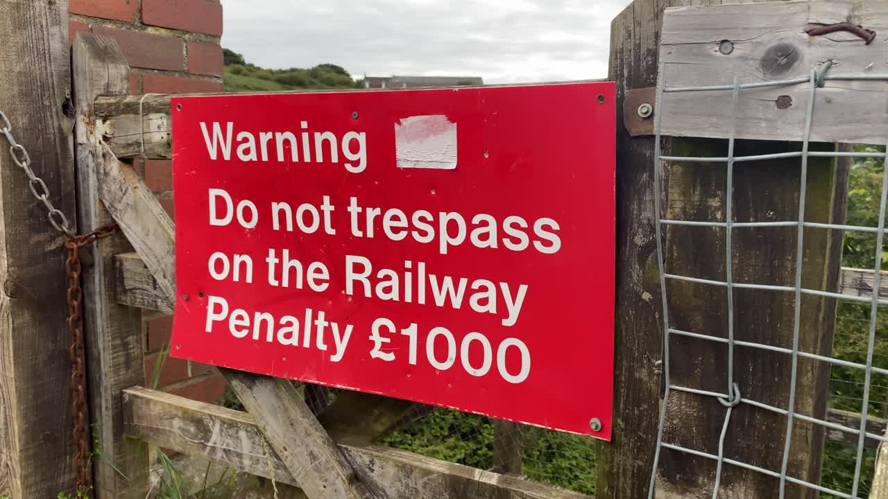 una señal roja al lado de una línea de ferrocarril advirtiendo a las personas que no entren en el ferrocarril
