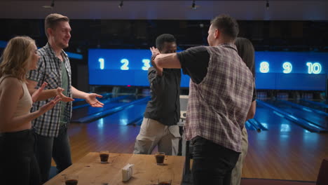 a black man in a bowling club happily lets five of his friends celebrate a knocked out streak. share the victory with friends. multi-ethnic group of friends