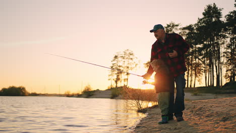 granddad is teaching his grandchild to fish on lake coast in sunset active weekend in summer