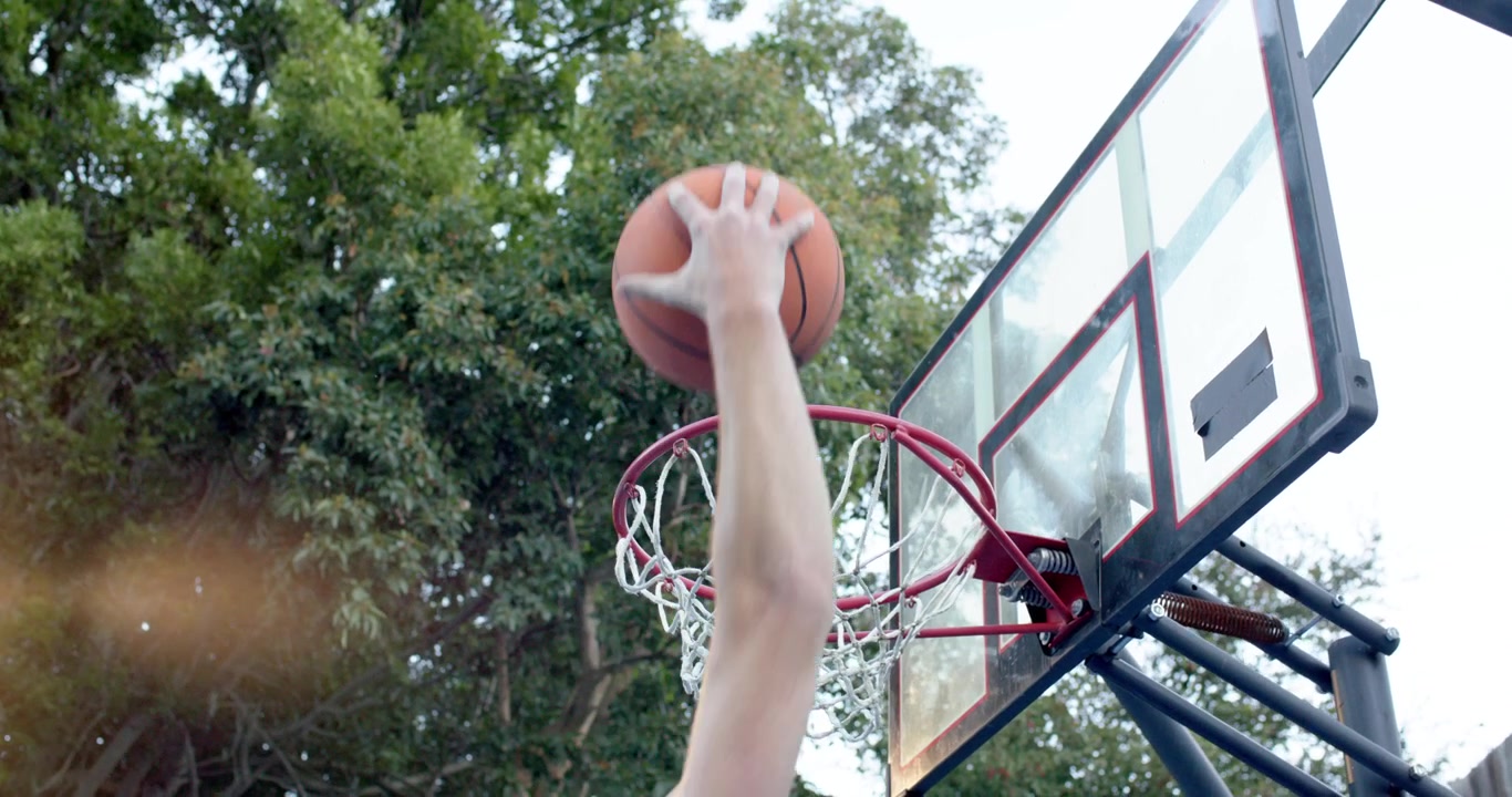 Un giocatore salta e mette la palla da basket nel canestro mentre la retina si tende durante una partita in cortile.