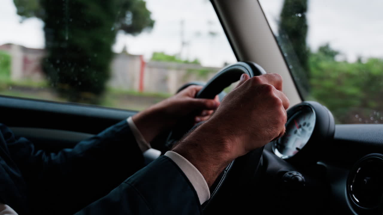 Close up of a man's hands on a steering wheel, driving a car on the road