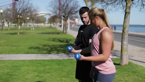 side view of focused woman training arms with dumbbells.