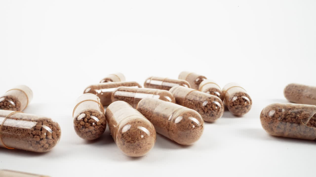 cápsulas múltiples transparentes llenas de polvo de hierbas marrón en una superficie blanca