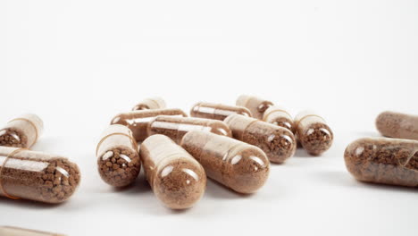 multiple transparent capsules filled with brown herbal powder on a white surface