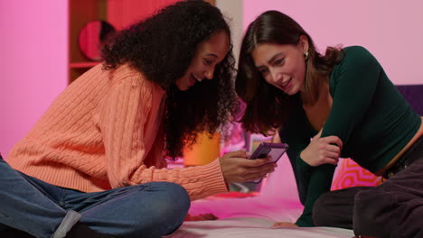 two women friends looking at a phone in a bedroom