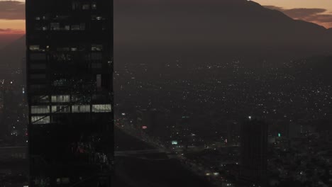 Aerial-revealing-shot-of-the-Cerro-de-la-Silla-from-behind-a-skyscraper-at-dusk