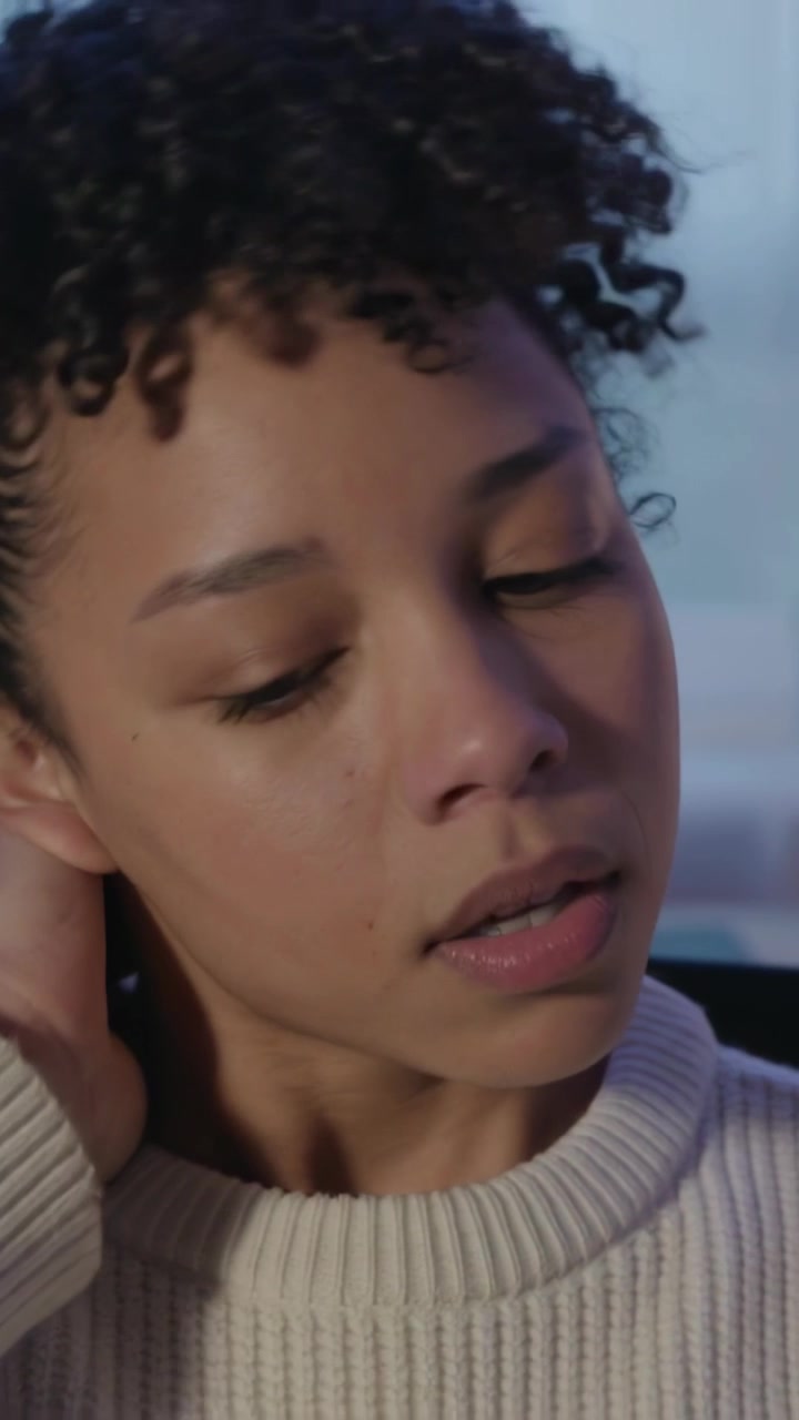 Vertical video: Rubbing neck, woman in ribbed top reacting to dusk light by window, seeking relief