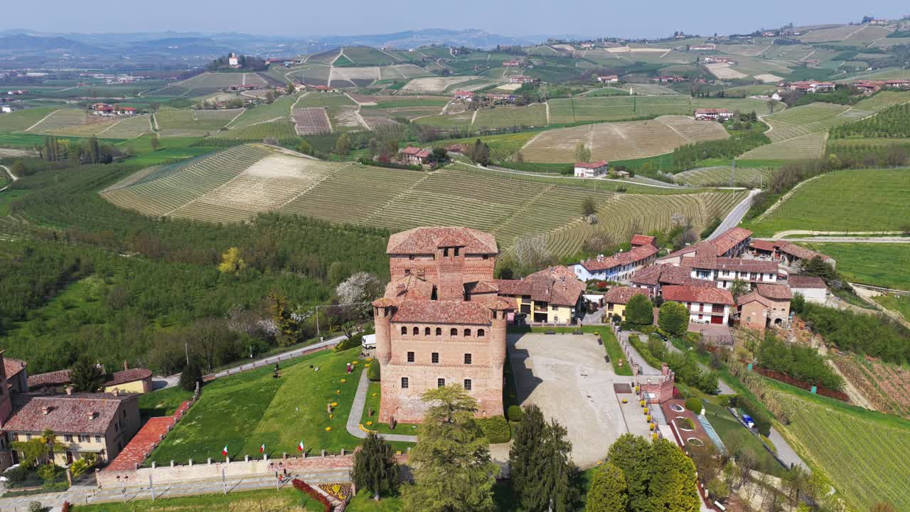 Reveal Dolly backward and tilt up aerial shot of Grinzane Cavour castle, revealing the historic architecture and surrounding vineyards of the Langhe hills