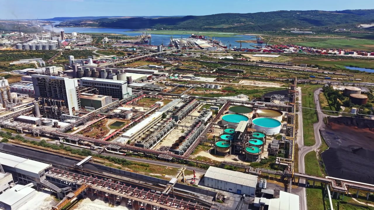 Zona industrial con fábricas y tanques de agua cerca de un río y colinas en un entorno diurno.