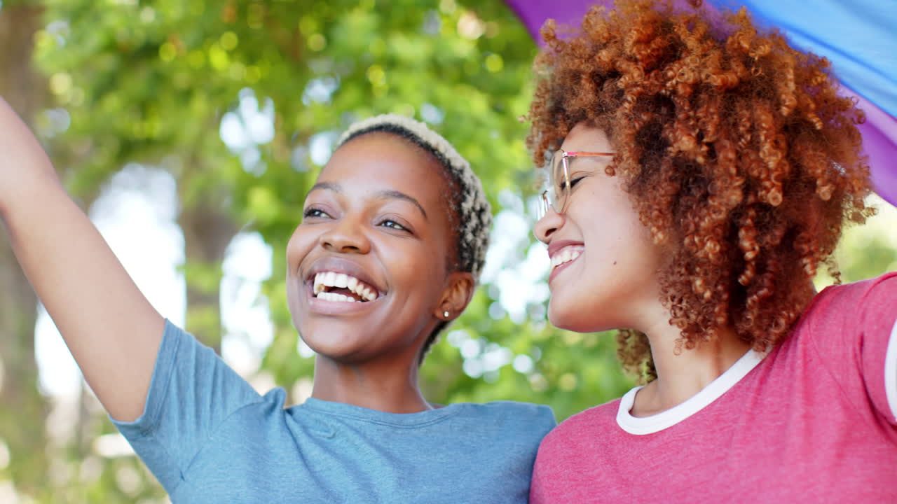 Happy diverse female lesbian couple embracing with rainbow flag of pride in slow motion