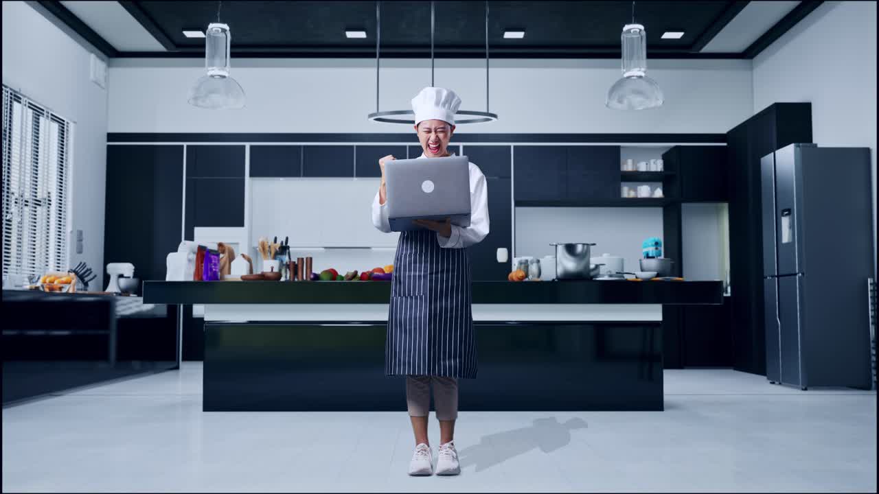 cuerpo lleno de mujer asiática chef mirando una computadora portátil luego gritando meta celebrando en la cocina de casa