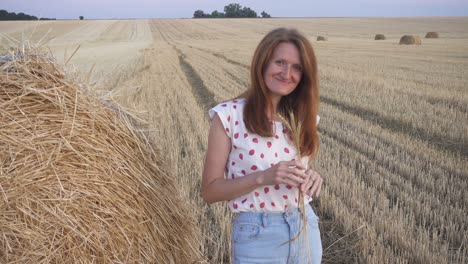 outdoor evening portrait of a beautiful young smiling girl near the round bale of hay in a wheat field