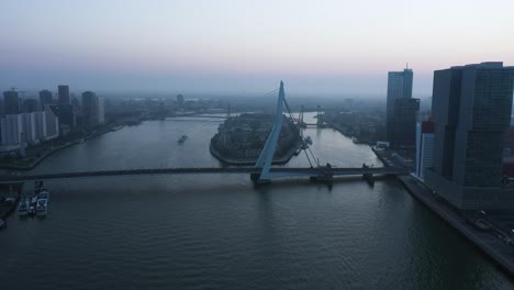 aerial backwards shot of erasmus bridge and river during foggy morning in netherlands