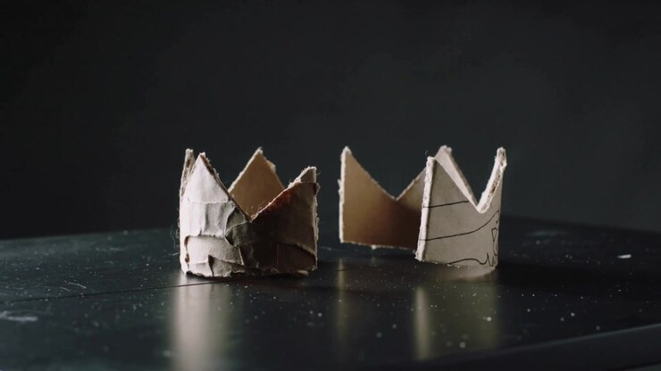 Cima frastagliata che si inclina facendo scivolare due segmenti di corona di cartone su un tavolo nero, mostrando del nastro adesivo