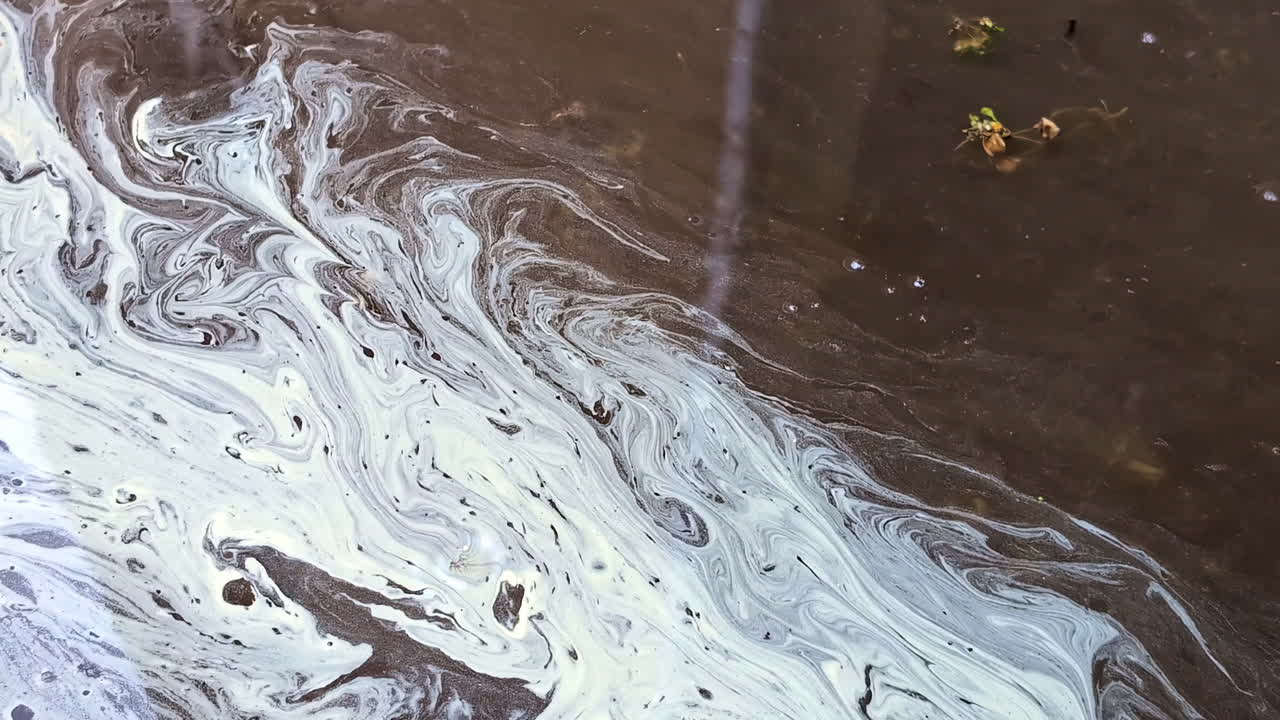 환경 오염을 강조하는 물 표면의 오염으로 인한 회전 패턴의 클로즈업