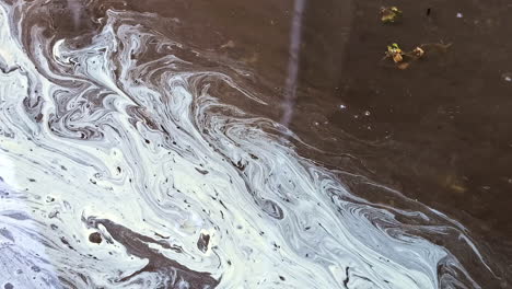 primer plano de los patrones de remolinos causados por la contaminación en la superficie del agua, destacando la contaminación ambiental