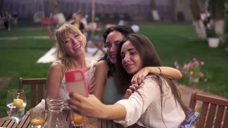 Carefree-Women-Chatting-In-Veranda-Cafe-Outdoors-Taking-Selfie-Photo-Or-Video-On-Smartphone