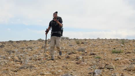 low angle shot of a hiker talking on a live video while walking on mount ramon desert trail on the way to ramon crater in the negev desert, israel at daytime