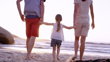 Familia-Feliz-En-La-Playa-Tomados-De-La-Mano-Balanceando-A-Una-Niña-Al-Atardecer-De-Vacaciones