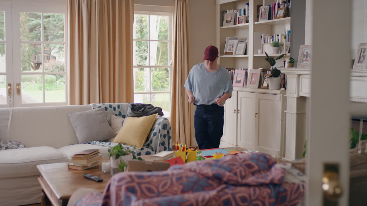 다운 증후군을 가진 재미있는 십대 소년이 거실에서 춤을 추고 재미있게 춤을 추고 어리석은 춤 움직임으로 축하하고 행복한 아이가 집에서 주말을 즐기고 있습니다.