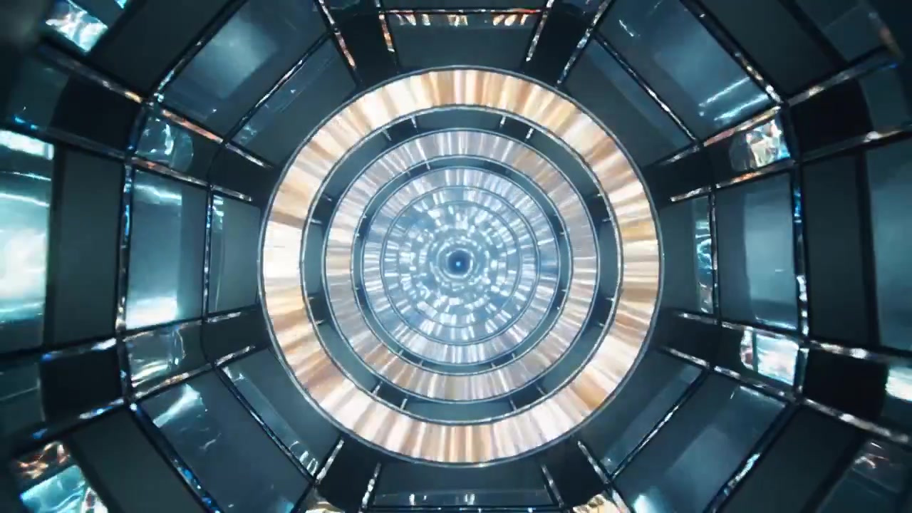 Sequenza di illuminazione che inizia con anelli concentrici che alternano blu e oro in un tunnel d'acciaio, formando un vortice.