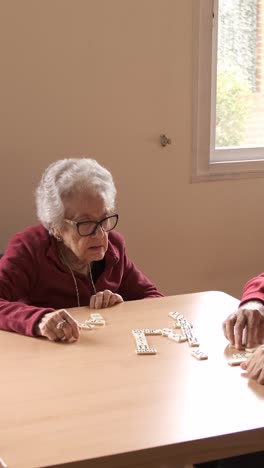 senior friends playing dominoes at table in nursing home