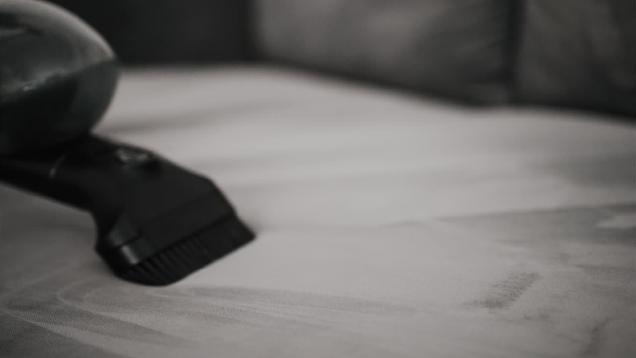 Detailní záběr malého vysavače, který čistí šedou pohovku