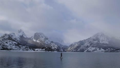 man on paddle board between water and mountains on coast