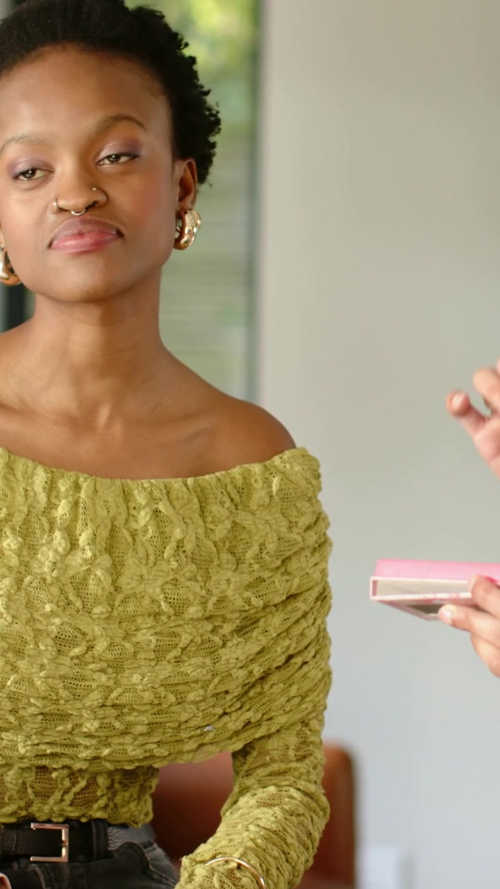 Vertical video: Following woman in olive top tracking hand with pink compact at lounge, deciding