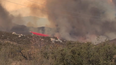 airplane drops red fire retardant on wildfire in