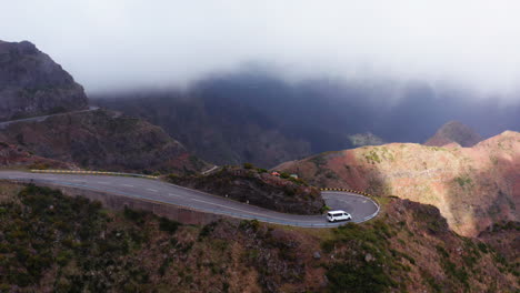 spectacular aerial tracking shot of van driving on dangerous curvy serpentines road in mountains during foggy day