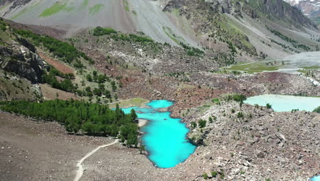 cinematic aerial shot of turquoise colored water in the mountains at naltar valley in pakistan, slow revealing drone shot