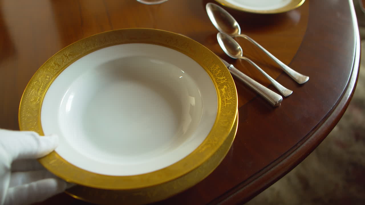 Professional server sets luxury gold rimmed soup plate with silverware at formal table. Ideal for upscale restaurant, catering, and hospitality service visuals