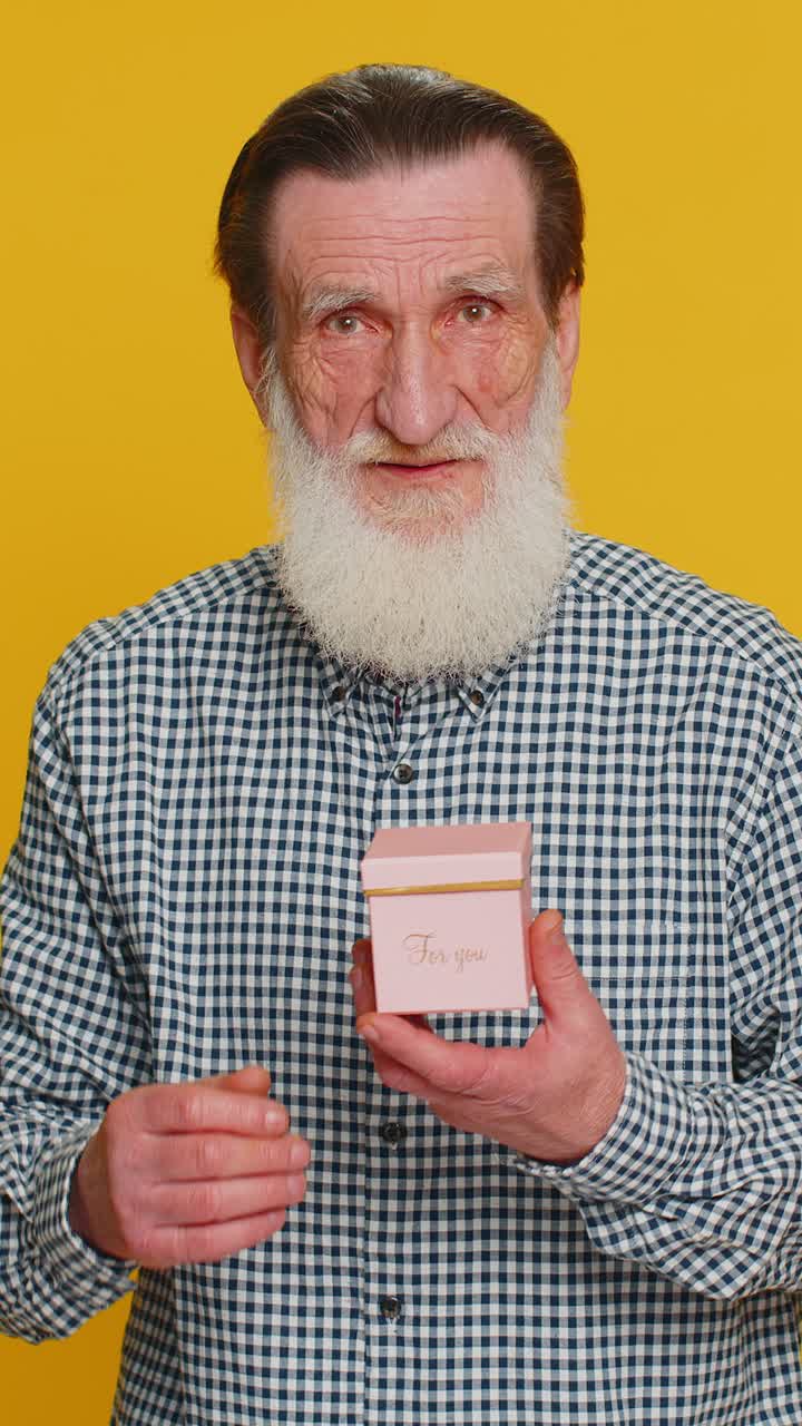 Smiling senior man presenting jewelry gift present box stretches out hands promotion discount sale