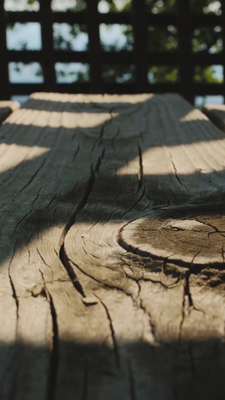 Vertical video: Sunlight through lattice shifting weathered plank, showing knot and grain on deck