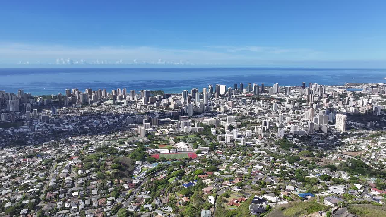 Aerial drone footage overlooking the Honolulu skyline on Oahu, Hawaii, showcasing high-rise hotels, tropical coastline, blue ocean waters, and the scenic cityscape of Waikiki under sunny skies