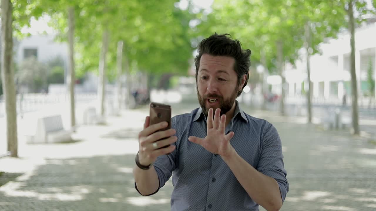 중간 감정성 성인 남자가 야외에서 비디오 통화 중에 이야기하고 있습니다.