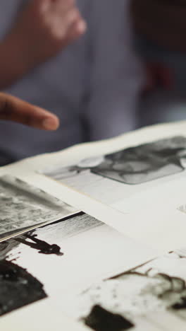 african-american guy looks at old family photo in large album with little girl and woman coworker at table during visit closeup slow motion