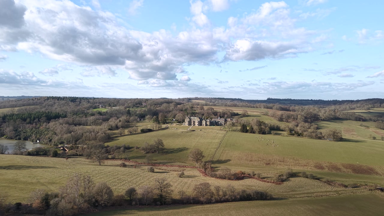 Aerial view over vast farming land towards majestic Bayham hall grand estate woodland grounds