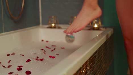 close up shot of woman's leg entering a hot bath with flowers and foam, interior