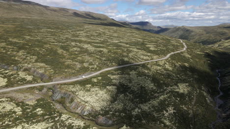 drone captures an aerial shot which shows a jeep driving along the picturesque empty road on the side of the green hill