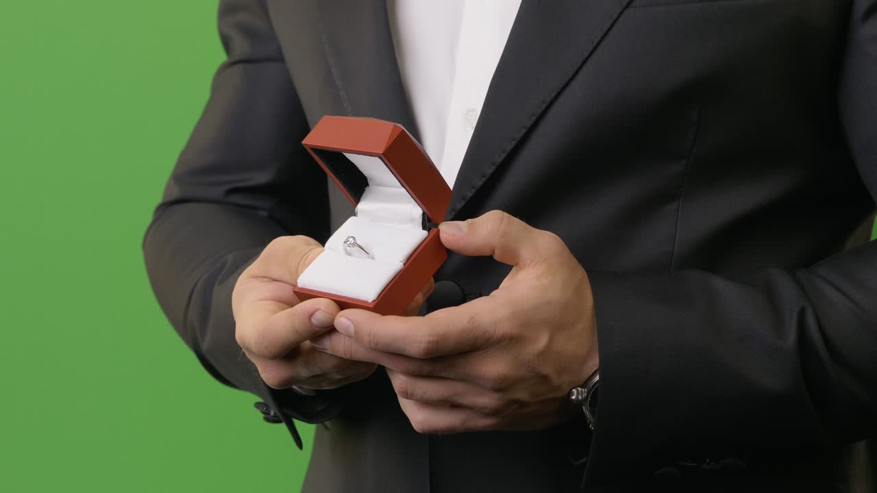 검은색 슈트를 입은 남자가 약혼 반지를 보여줍니다.