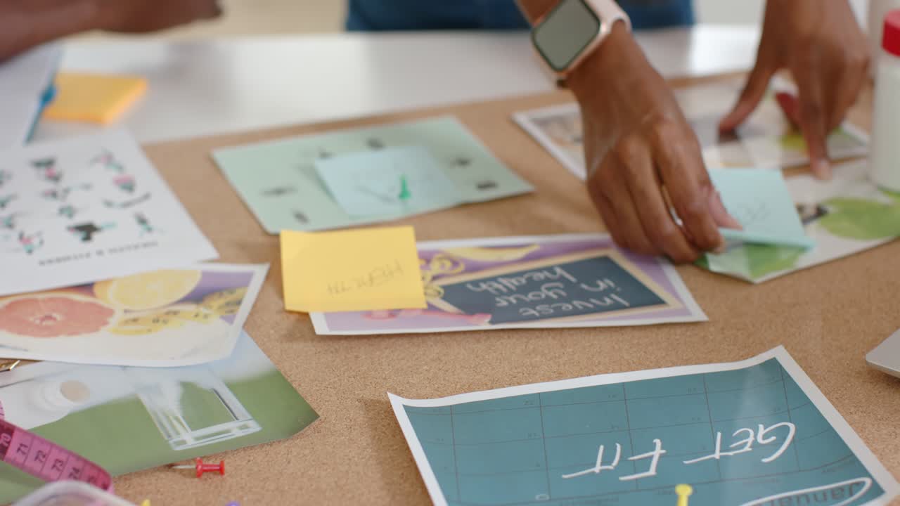 African American team arranging corkboard on table for planning, smoothing prints and pinning notes