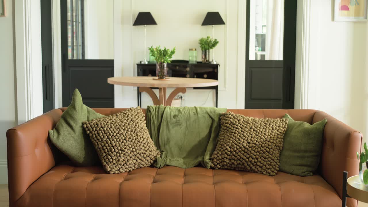 Camera is pulling back and tilting upward, revealing living room behind brown tufted leather sofa