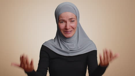 muslim woman in hijab smiling friendly at camera, nods her head gesturing hello hi, assalamu alaikum