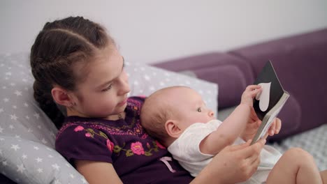 little brother reading book with sister. newborn baby in sister embrace